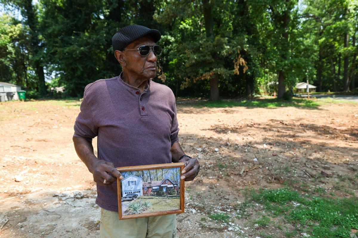 Thomas Stevenson holds a photo of his mothers’ house, which used to be on the empty lot behind him. When the financial burden of taking care of his mother’s home, as well as his own, became too much to keep up with he decided it was time to sell.