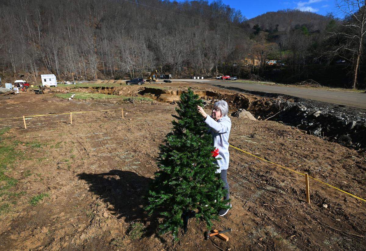Christine Skowronski begins to decorate a Christmas tree at Sharon Hughes’ property in Burnsville on Monday. Sharon Hughes had to flee her over 100-year-old home as the heavy rain from Hurricane Helene caused the Cane River to overflow its banks.
