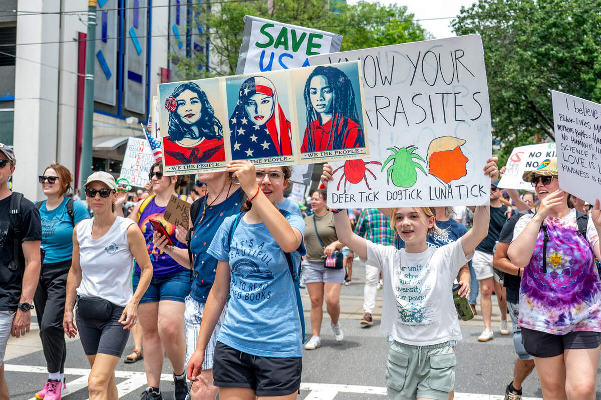 Ada Lee Smith and Celia Kaul hold up signs as the march at the No Kings march and rally in Charlotte Saturday, June 14, 2025.