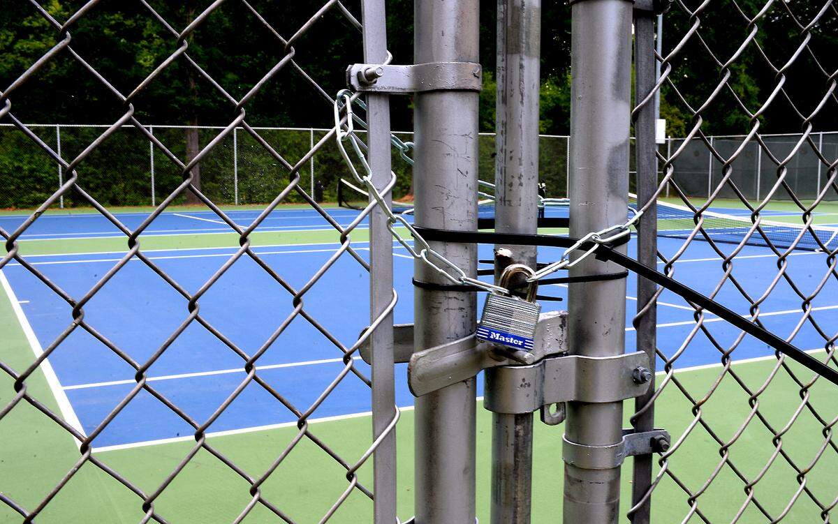 A padlock and zip tie lock the gate to a tennis court at Freedom Park on Wednesday, April 29, 2020. On Tuesday, April 28, 2020 it was announced that Meck County would be loosening restrictions on some businesses and recreational activities. 