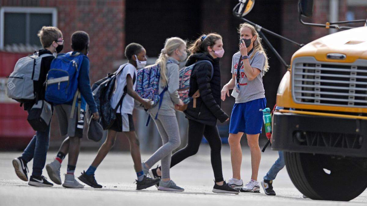 A teacher supervises students as they board a bus at the end of the day at Ballantyne Elementary School on Tuesday, March 9, 2021.