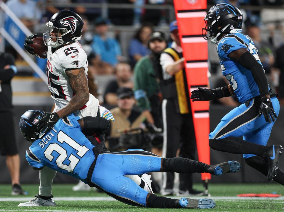 Panthers safety Nick Scott, bottom, hangs on while Falcons runningback Tyler Allgeier drags him along the turf as teammate Xavier Woods chases during the game at Bank of America Stadium in Charlotte, NC on Sunday, Oct. 13, 2024.