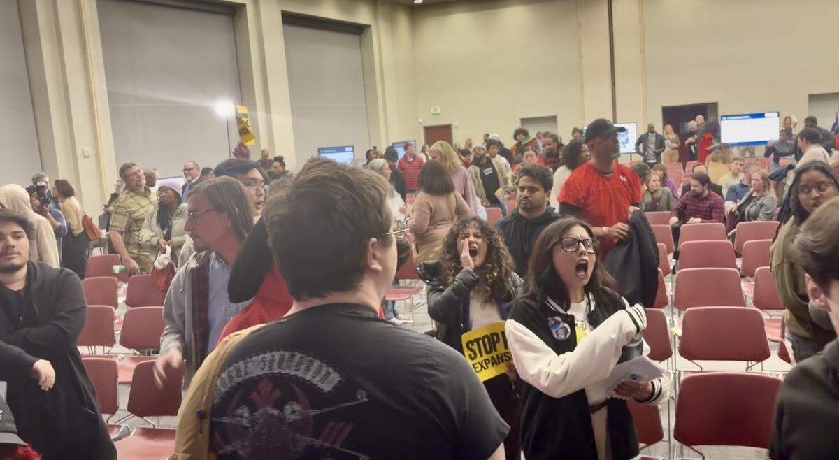 Participants shout “Let us speak!” at a town hall meeting discussing North Carolina Department of Transportation’s I-77 South Express Lanes project.