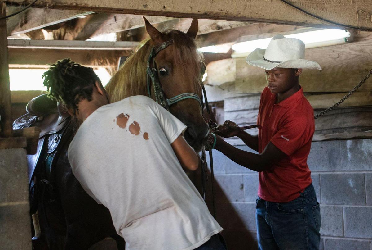Sixteen-year-old Malachi (right) hooks up a horse to his stable to prepare to wash the horse at Big M stables on Thursday, July 29, 2021.