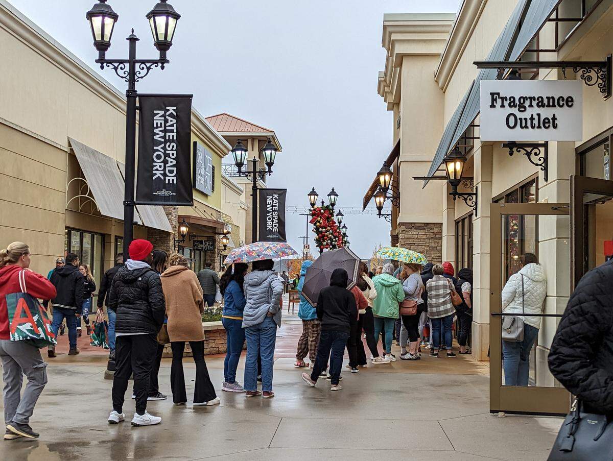 Lines formed outside designer stores like Kate Spade New York at Charlotte Premium Outlets after opening on Black Friday despite rain.