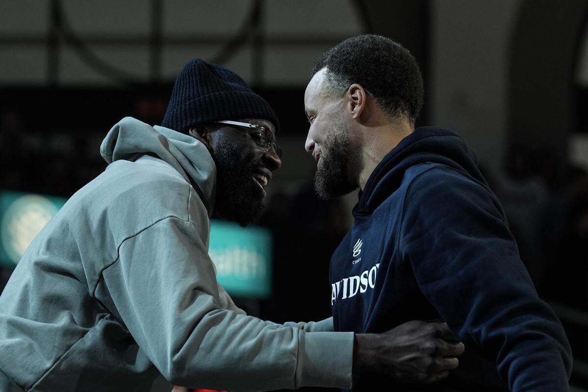 Golden State Warrior guard and Davidson alumni Stephen Curry, right, embraces teammate Draymond Green during halftime of an NCAA college basketball game between Davidson and Duquesne, Tuesday, Dec. 30, 2025, in Davidson, N.C.