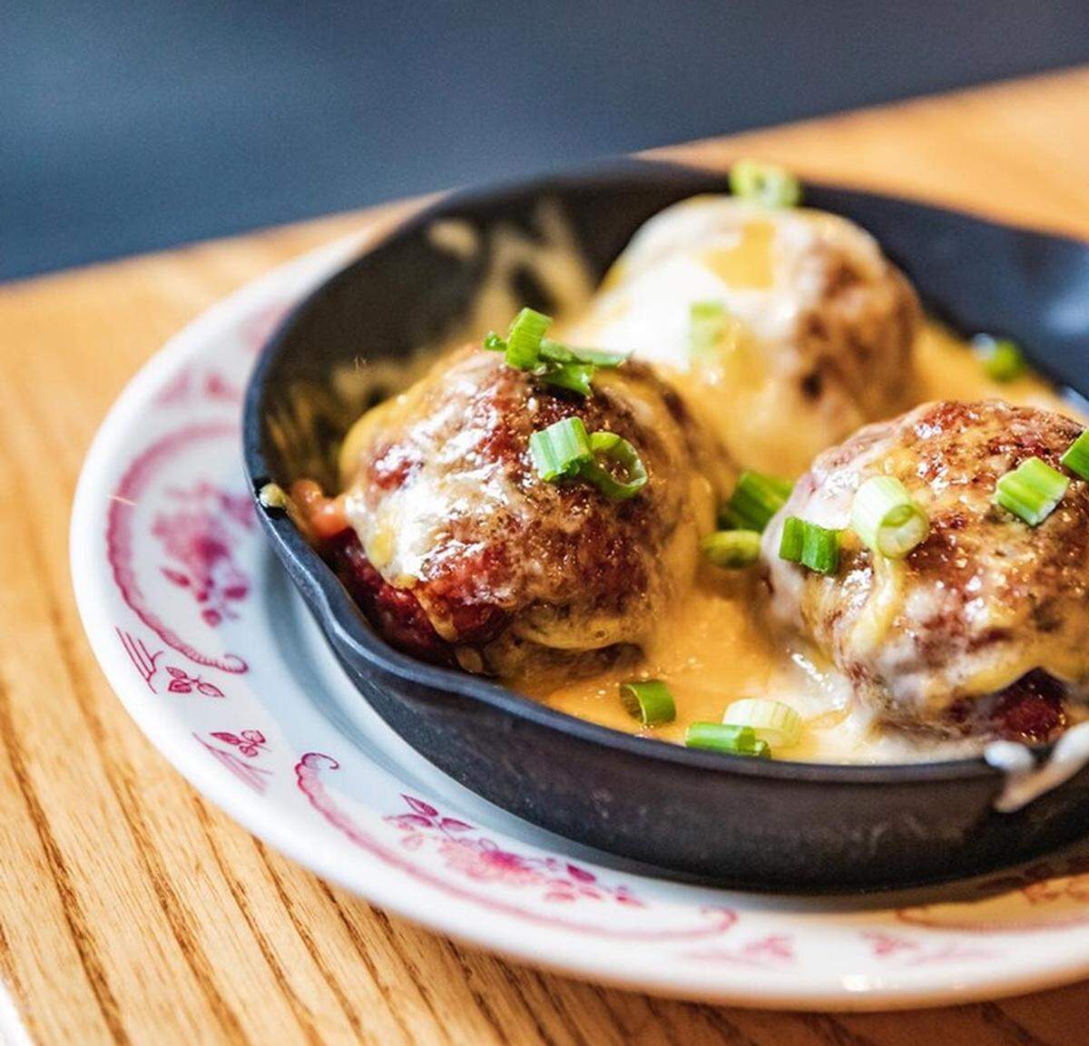 The Smoked Meatballs appetizer is topped with smoked jalapeño BBQ sauce, mixed melted cheese and green onion..