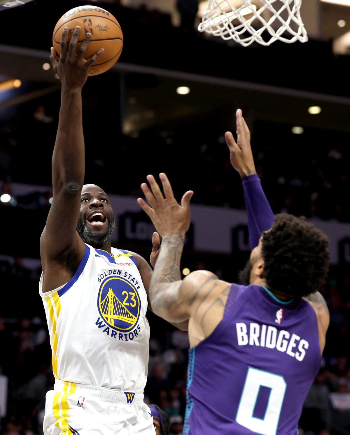 Golden State Warriors forward/center Draymond Green, left, releases a one-handed shot over Charlotte Hornets forward Miles Bridges, right, during action at Spectrum Center in Charlotte, NC on Monday, March 3, 2025.