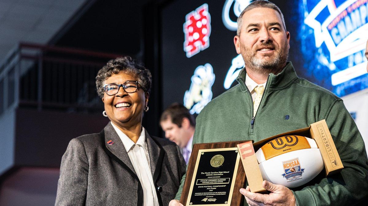 Northern Nash’s football coach Andrew Farriss accepts a football and plaque next to NCHSAA commissioner Que Tucker at a NCHSAA press conference about state championship games in Charlotte, N.C., on Monday, December 5, 2022.