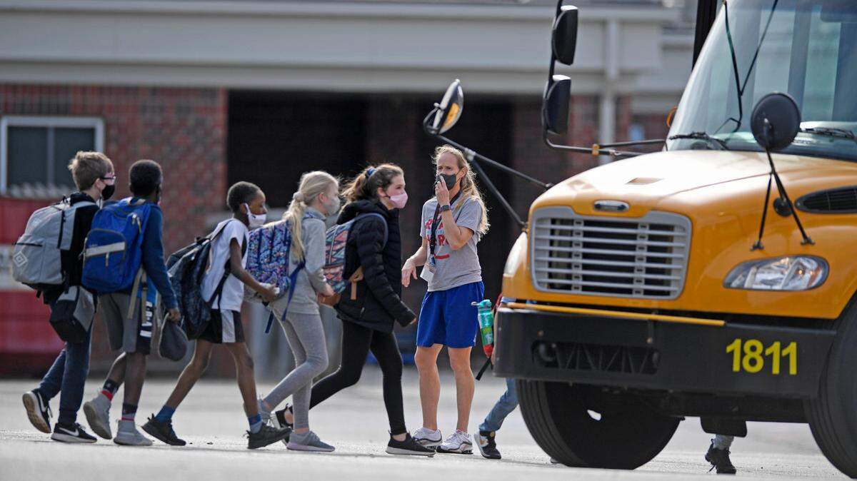 A teacher supervises students as they board a bus at the end of the day at Ballantyne Elementary School on Tuesday, March 9, 2021.