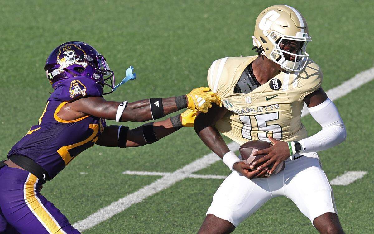 Charlotte 49ers quarterback Deshawn Purdie, right, fights to maintain his footing as East Carolina Pirates defensive back Ja’Marley Riddle, left, attempts a sack during action on Saturday.