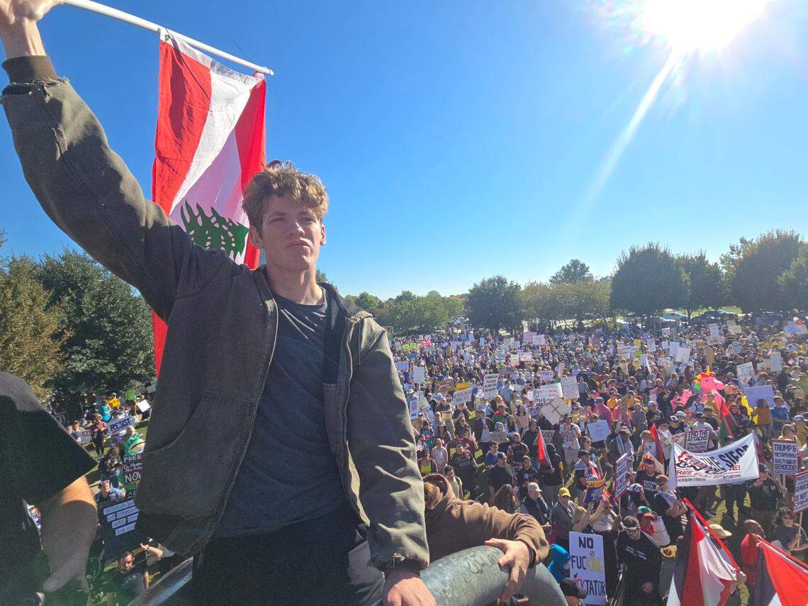 A protester hoists a Lebanese flag at the No Kings rally in uptown Charlotte on Saturday, Oct. 18. Hundreds crowded into First Ward Park before marching through Uptown.