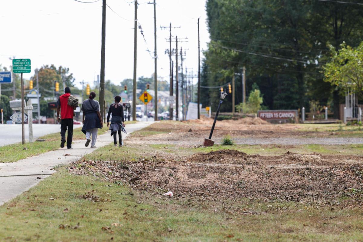 Piles of dirt and wood chips lie in spaces where mature oak trees once stood on West Sugar Creek Road as people walk by.