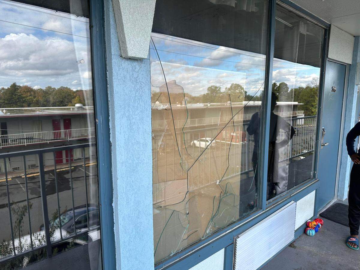 The window of a room at the Lamplighter Inn where a tenant has tried to patch it up with a piece of cardboard and drywall. There appear to be three bullet holes.