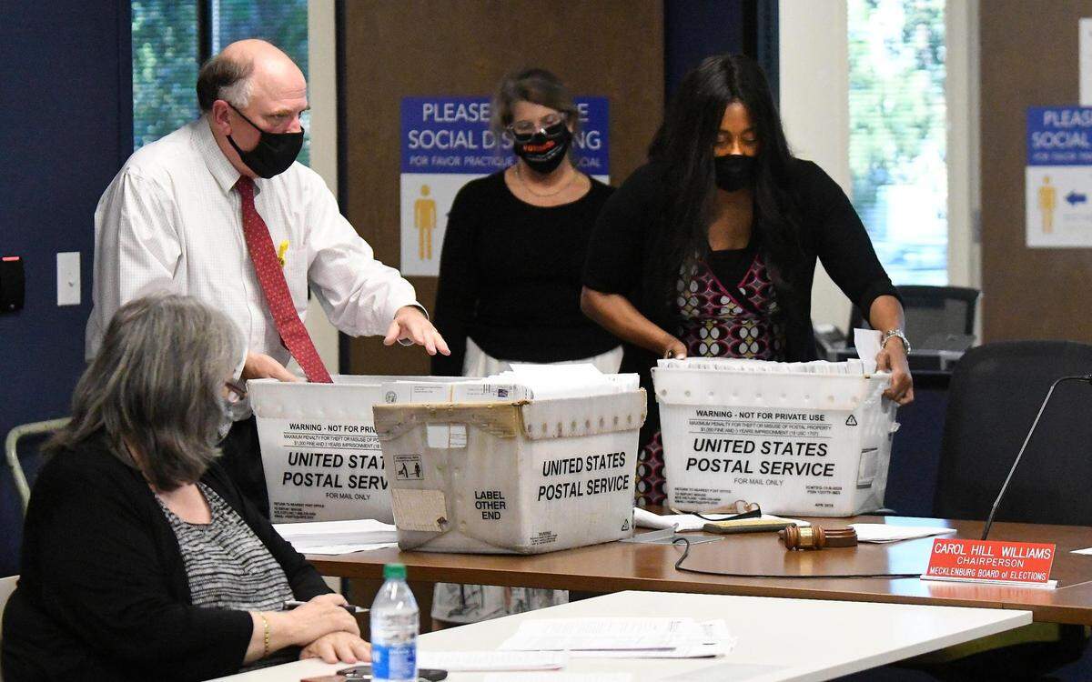 Michael G. Dickerson, left, Mecklenburg County Director of Elections and Kristin Mavromatis, center, assistant elections director, deliver a.basket of ballots to Carol Hill Williams, Chair of the Mecklenburg County Board of Elections for checking at the Board of Elections on Tuesday, October 6, 2020.