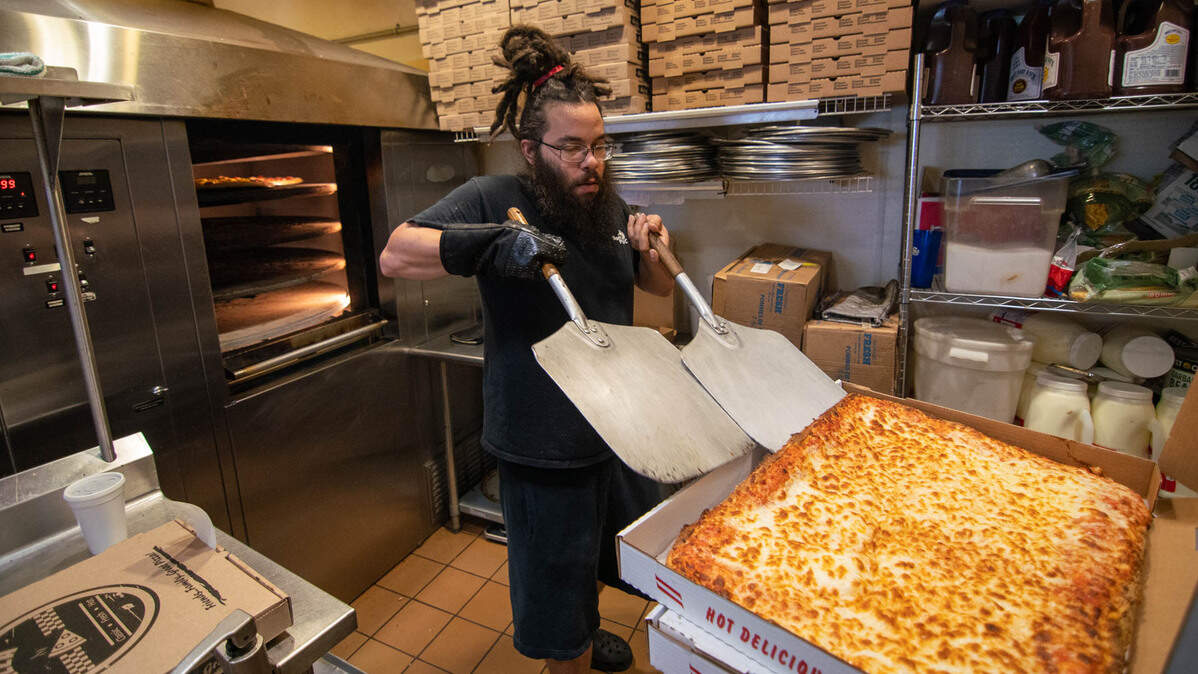 A Bisonte Pizza Co. cheese sheet pizza being cut just out of the oven.