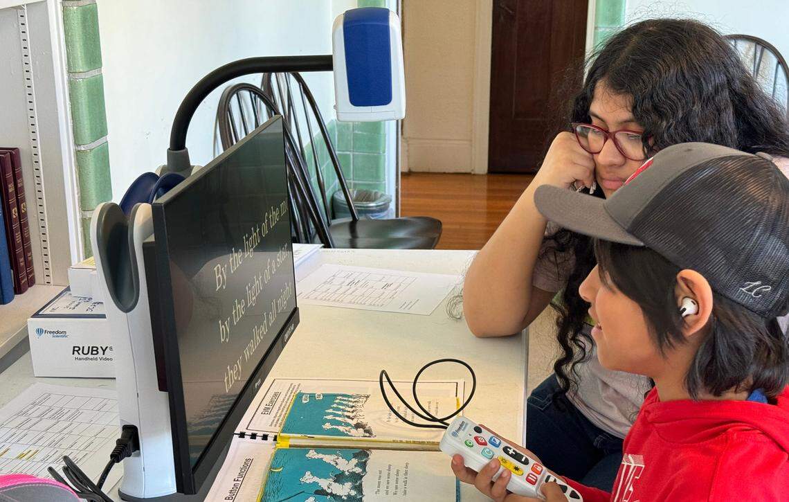 Juan Juarez Reyes, foreground, and his older sister Selena Juarez Reyes try out a portable desktop magnifier.