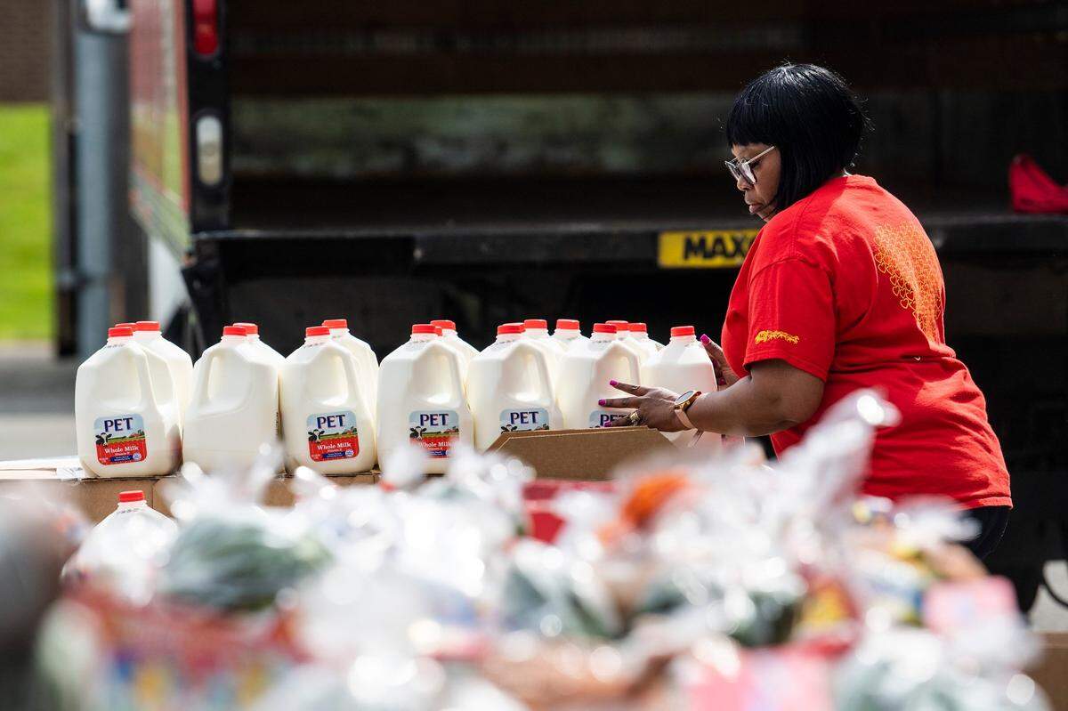 A volunteer from Wells Fargo arranges gallons of milk for food distribution by Loaves and Fishes at a YMCA in Charlotte, North Carolina. As prices rise, groceries and other goods become harder for low-income people to buy.