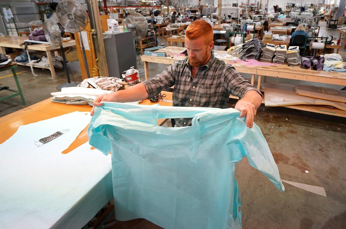 EJ Victor Furniture CEO/COO David Bennett examines one of the medical gowns the company is now producing on Friday, March 27, 2020. The furniture maker has begun producing medical gowns, mask covers and a triage cot to help in the fight against the Coronavirus.