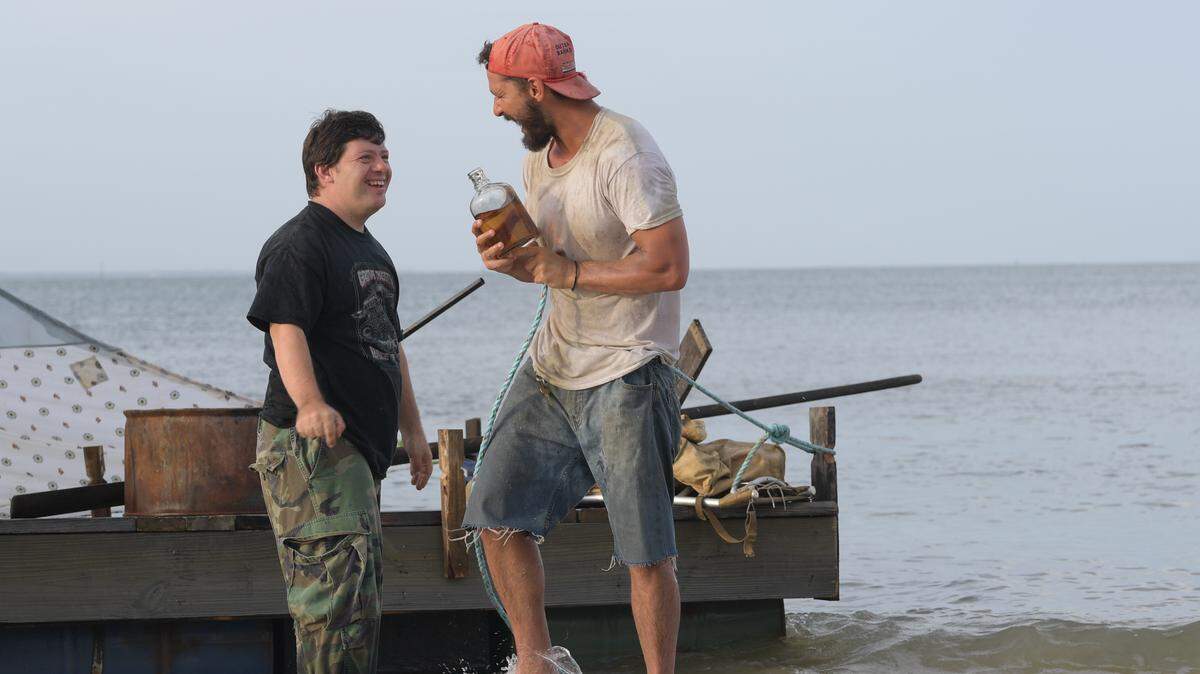 Zak (Zack Gottsagen), left, and Tyler (Shia LaBeouf), right, near a raft they built in “The Peanut Butter Falcon”.