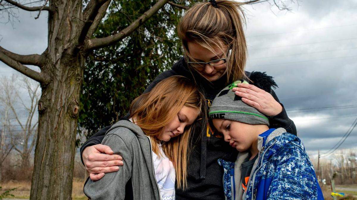Vanessa LaBrie holds onto her two children, Kiersteyn Fields, 10, and brother Landon Baker, 8, as they stand in their yard near Oxford High School on Dec. 2, 2021 in Oxford, Mich. A 15-year-old sophomore opened fire at the school on Nov. 30, killing four students.