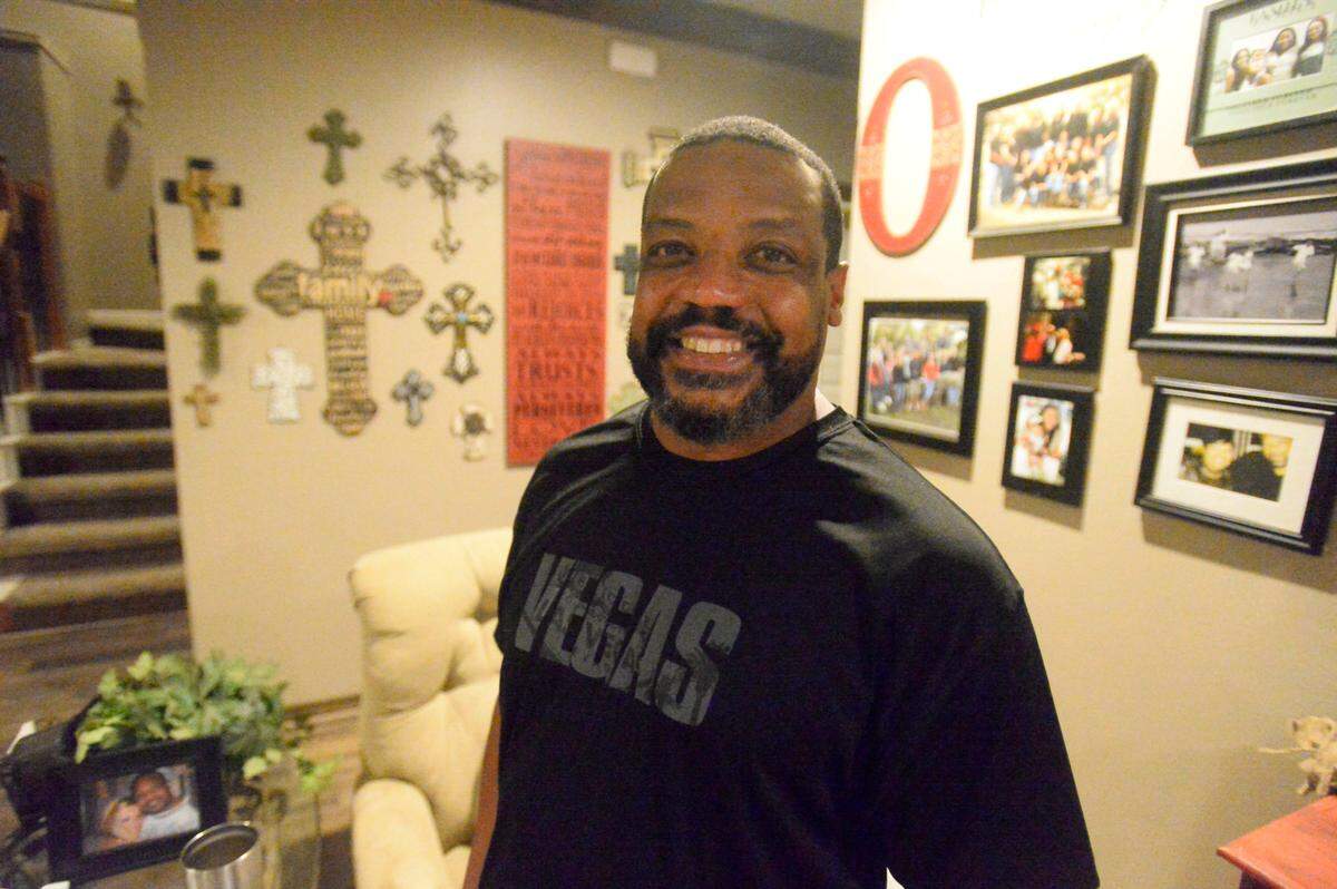 Former Carolina Panthers player Winslow Oliver stands in his living room in Richmond, Texas, surrounded by family photos and crosses representing his Christian faith.