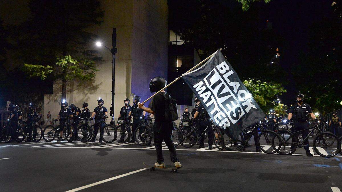 A protester carries a Black Lives Matter flag as he skateboards in front of Charlotte-Mecklenburg police officers along College Street in Charlotte during an August 2020 protest.