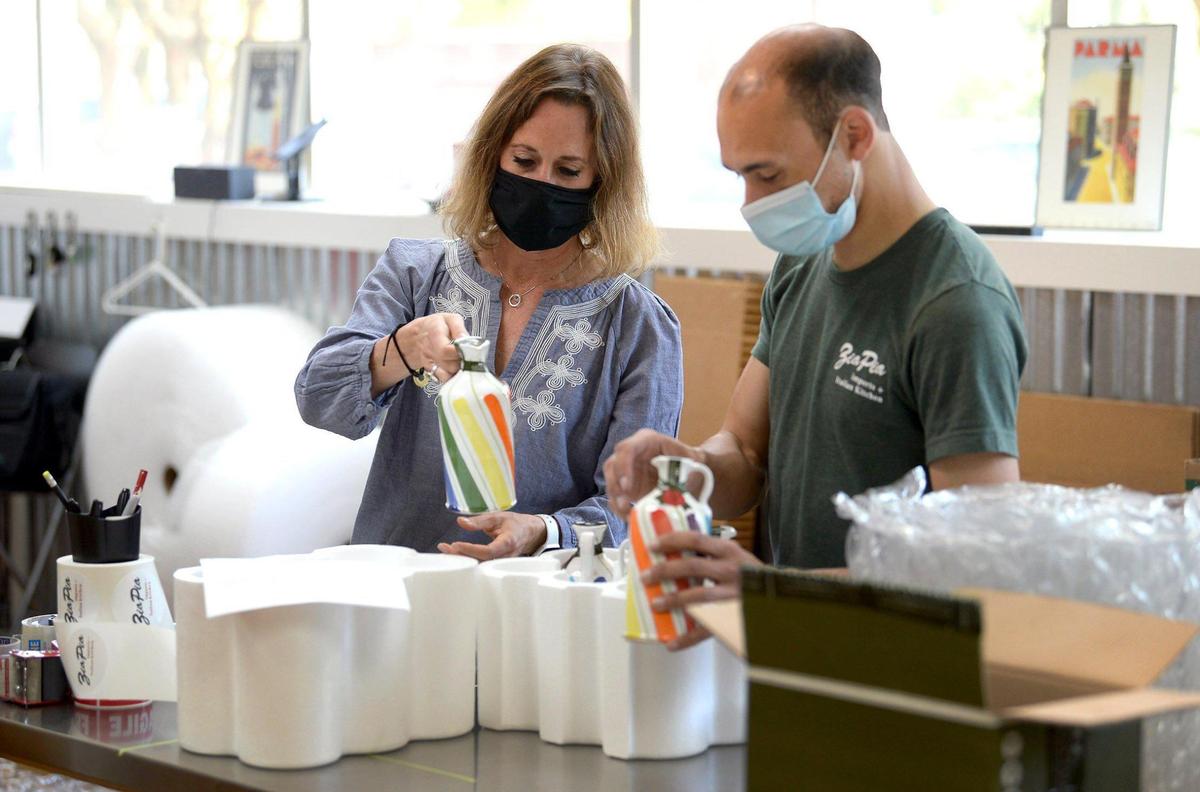 Victoria Custodi, owner of Zia Pia Imports + Italian Kitchen, left, looks at one of the businesses hand-painted ceramic olive oil containers with employee James Jordan Wednesday at the warehouse in Charlotte.