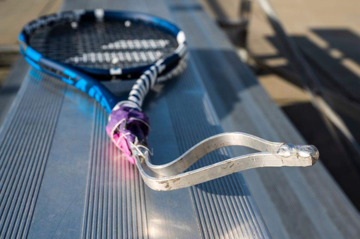 One of Gaila Fosbinder’s rackets sits on a bench as she practices tennis with her coach at Queens Tennis Center in Mario Diehl Park on Friday, February 25, 2022 in Charlotte, NC. The customized racket has the handle cut off with an aluminum insert that goes into the frame and is held in place with epoxy. Fosbinder then inserts her whole hand into the aluminum portion of the racket, along with a plastic she melts down to make it a tighter fit. The racket is then taped to her hand to ensure that there is no slippage when she swings.