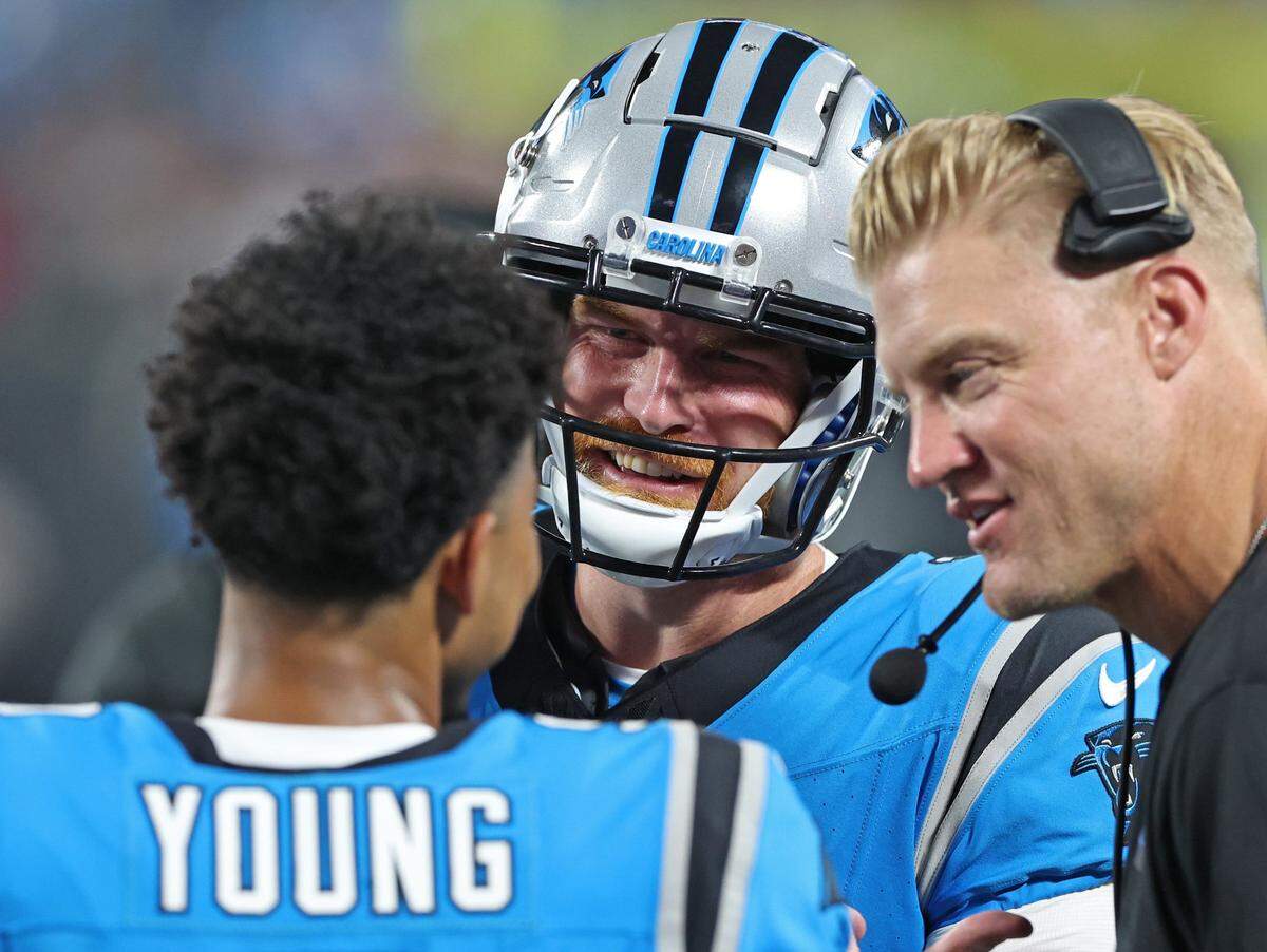 Carolina Panthers quarterback Bryce Young, back to camera, talks with quarterback Andy Dalton, center, and quarterbacks coach Josh McCown, right, during second quarter action against the Detroit Lions on Friday, August 25, 2023 at Bank of America Stadium in Charlotte, NC.