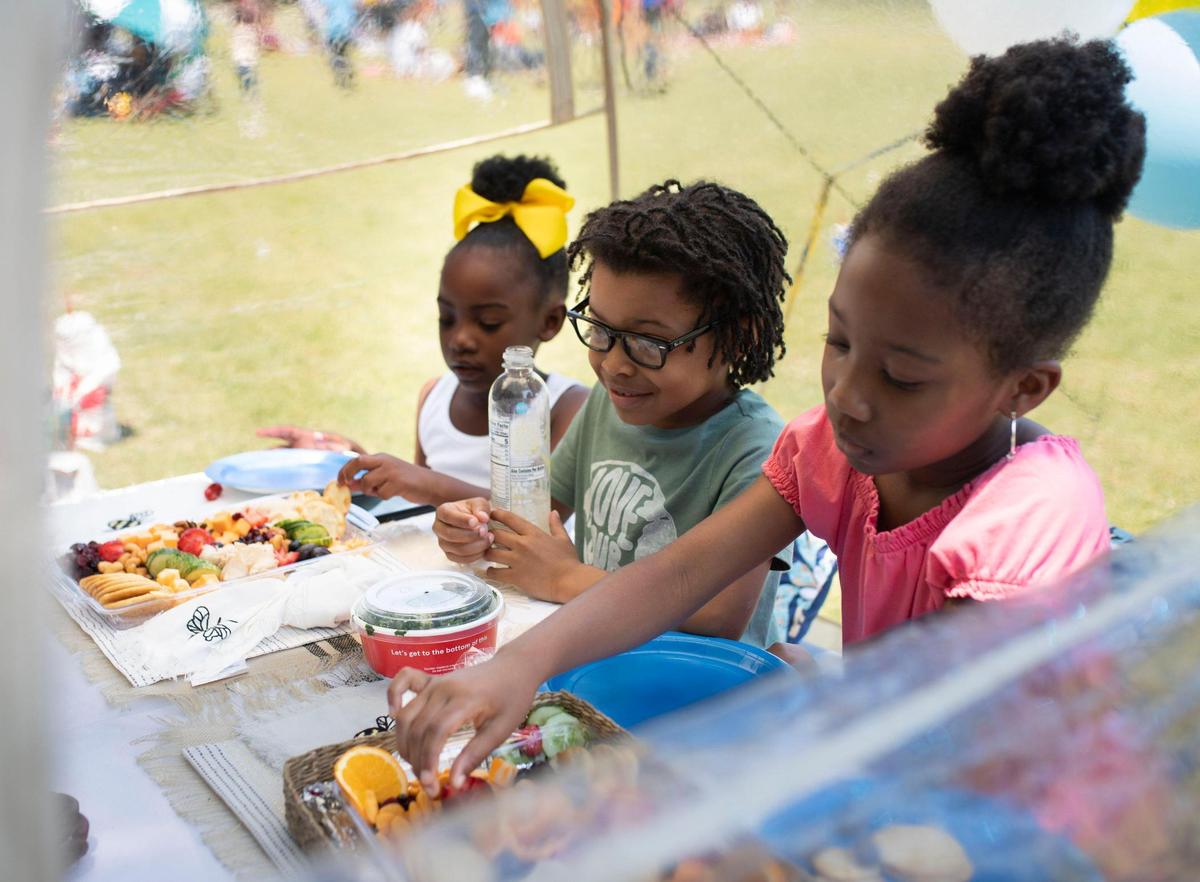 Students Azi Tillman, left, King Anderson, center, and Gioanna Mayfield, from Elizabeth Traditional Elementary School, hangout under a tent during the school’s picnic celebrating the last day of school at Independence Park on Friday, June 9, 2023.