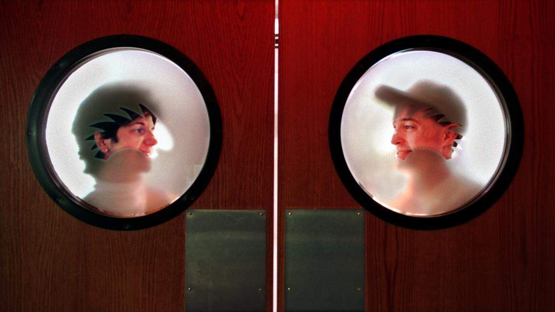 Two people, one on the left and one on the right, look at each other in front of circular, frosted glass portholes set into dark wood doors. The person on the left has short, dark hair and the person on the right is wearing a baseball cap. Their faces and shoulders are visible as blurred, backlit silhouettes and they are framed by their Porcupine logo.