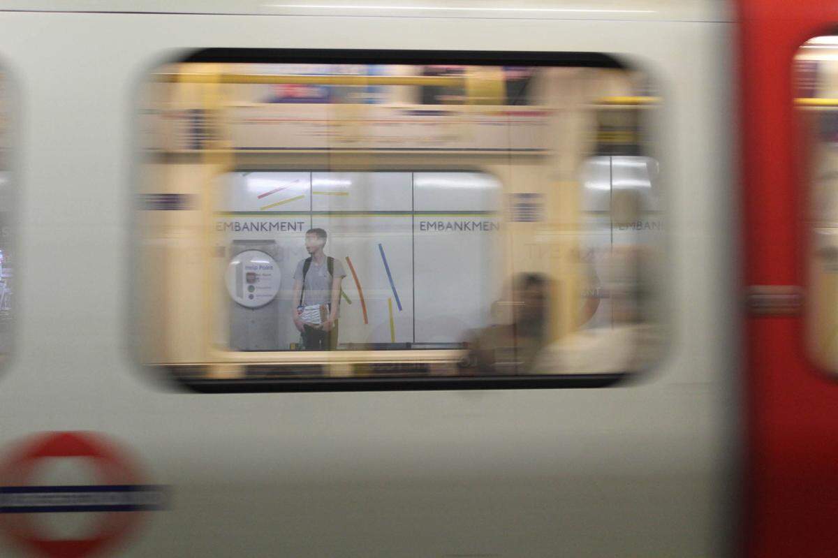 Title: Through the Glass: Longing at a Crossroads Caption: Man stands, framed by moving train in the London Underground in June 2023.