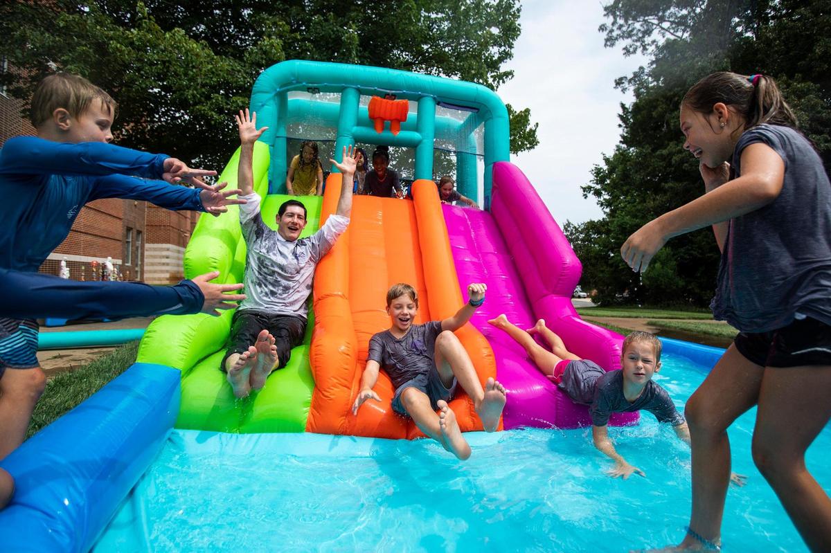 Dr. Gregory Monroe, second from left, joins kids in going down an inflatable water slide at a summer camp at St. Matthew Catholic School last week.