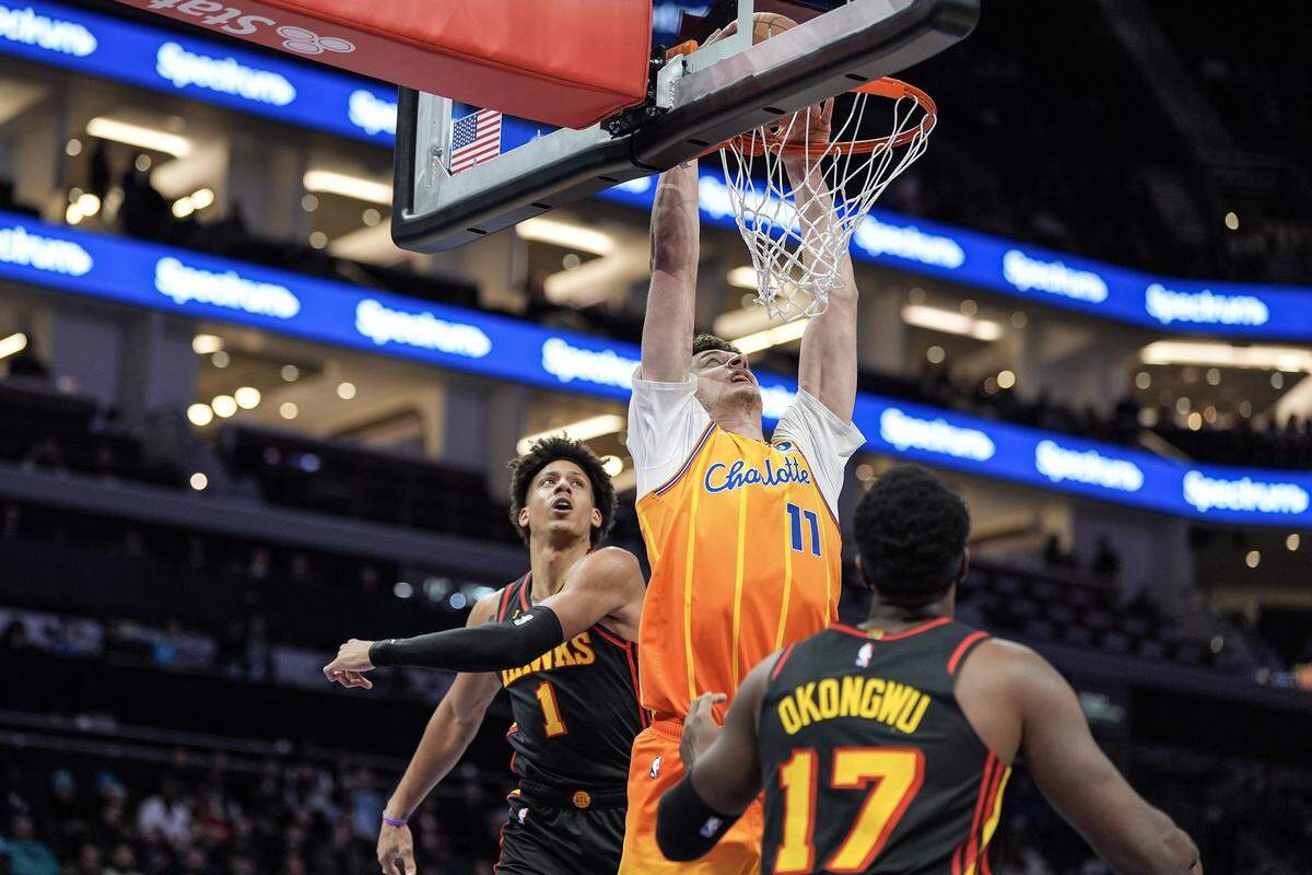 Charlotte Hornets center Ryan Kalkbrenner (11) drives between Atlanta Hawks forward Jalen Johnson (1) and  forward Onyeka Okongwu (17) for a slam dunk during the first half of an NBA basketball game, Thursday, Dec. 18, 2025, in Charlotte, North Carolina.