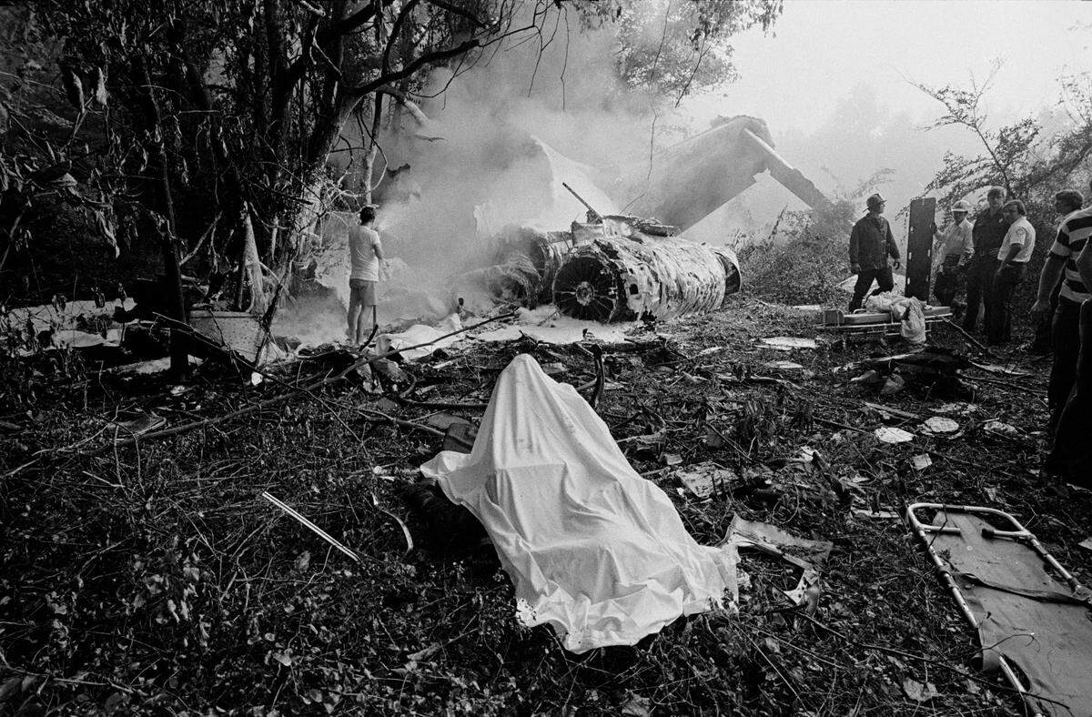 A shroud covers the body of an Eastern Flight 212 victim still strapped to an airplane seat in the aftermath of the plane crash on Sept. 11, 1974. The plane’s tail section smolders in the background.