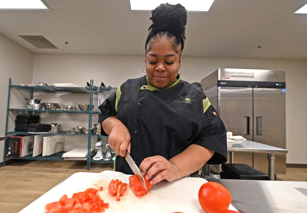 Carlotta Knox cuts tomatoes in a classroom at FeedNC on Tuesday, October 24, 2023. Knox is part of the workforce development program at feedNC. FeedNC formerly known the Mooresville Soup Kitchen relies 100% on community donations to provide breakfast, lunch and groceries to people in need each week day. FeedNC offers culinary and warehouse jobs. The program’s classes are 12-week programs.