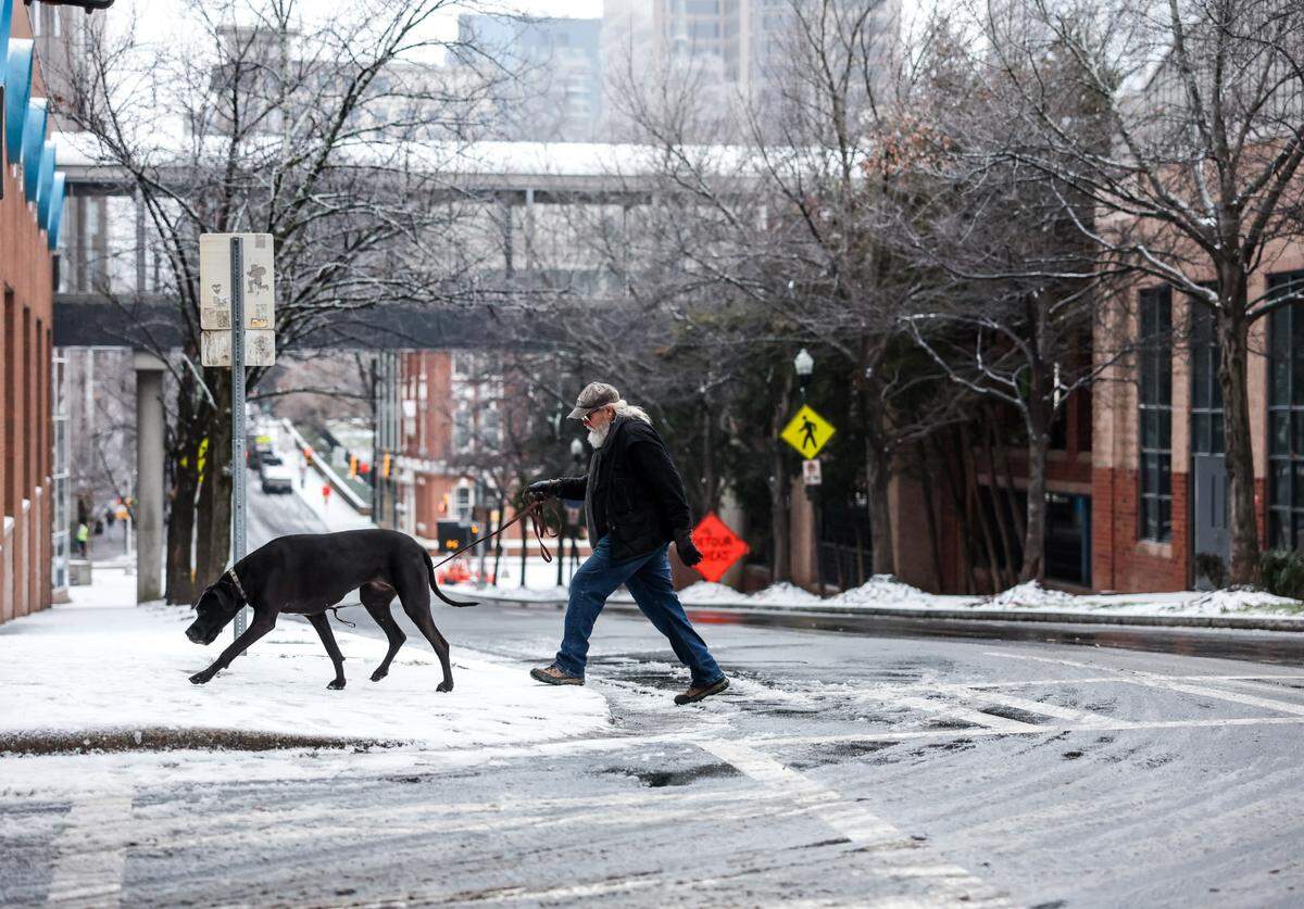 A man and his dog cross an ice-covered Church Street in Uptown after a winter weather front brought rain, snow and sleet into the area on Jan 23.