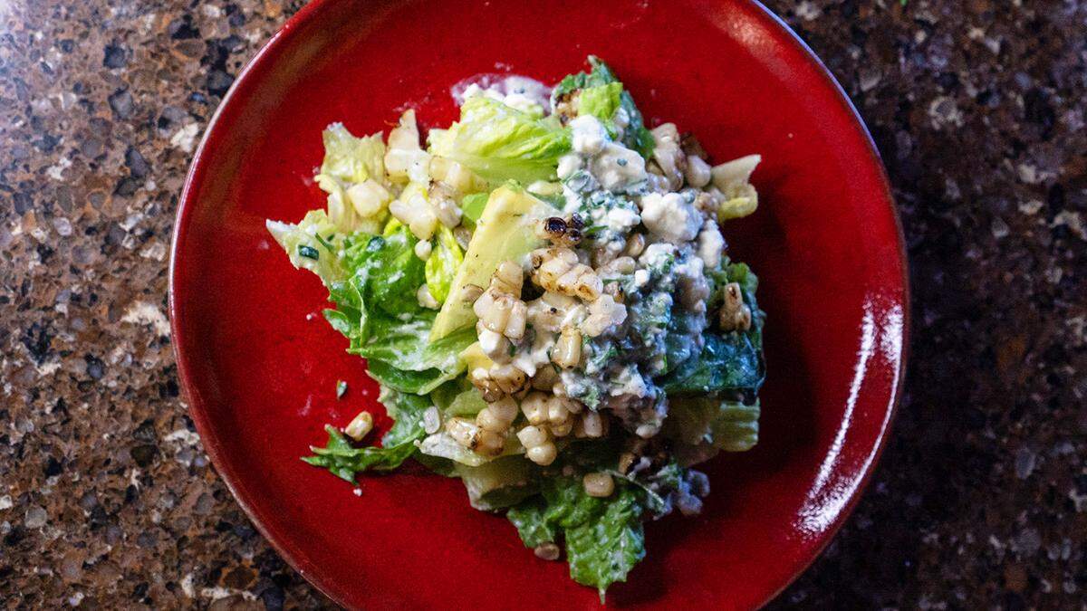 Corn and avocado salad topped with feta dressing on a red plate.