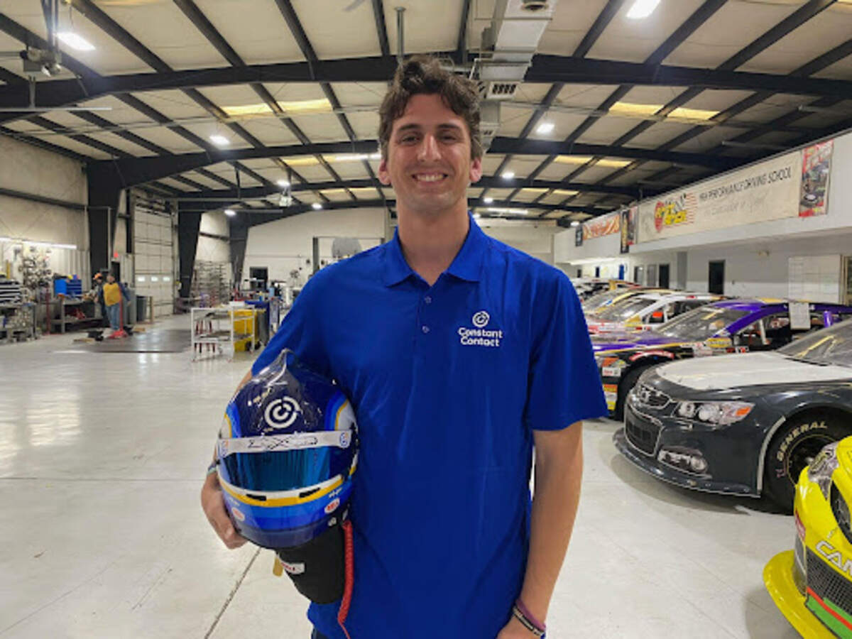 At the race shop ahead of his start at Charlotte Motor Speedway, Jayson Alexander poses with his helmet in the colors of his sponsor, Constant Contact.