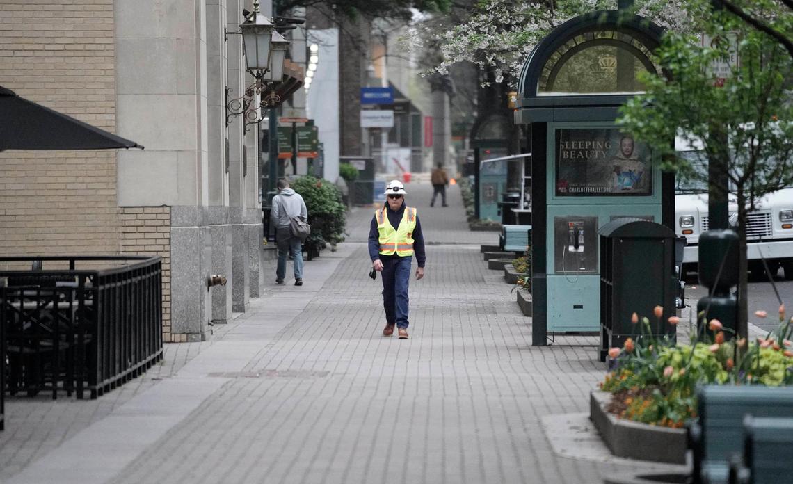 A worker walks along a deserted sidewalk along Tryon Street around 8 a.m. in uptown Charlotte in the wake of the coronavirus pandemic on Tuesday, March 24, 2020.