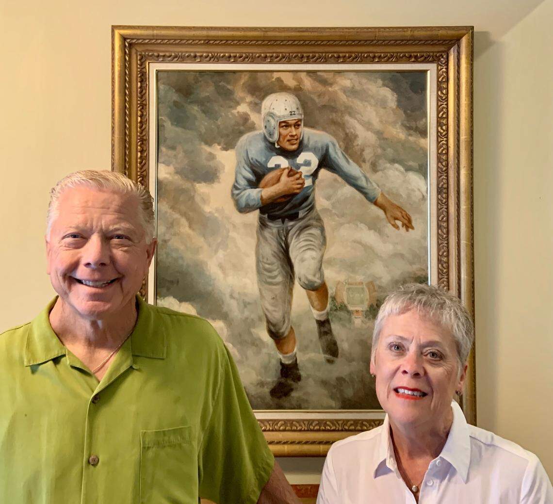 Barbara Justice Crews (right), the daughter of former UNC football star Charlie “Choo Choo” Justice, poses along with her husband Billy Crews in August 2020 at their home in Cherryville, N.C., in front of a painting of her famous father. Charlie Justice died in 2003.