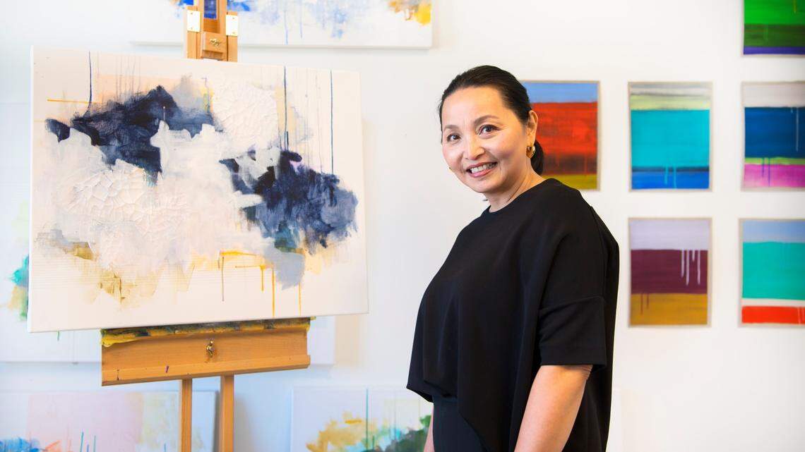 Charlotte artist Malu Tan is an abstract expressionist. Here she poses with a work in progress from her Color Collage series (left). To her right are small pieces she paints to help her figure out which color combinations to use.
