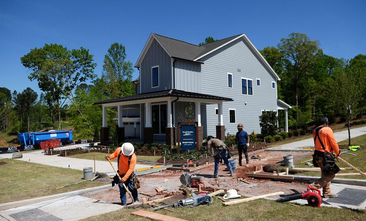 Workers finish a sidewalk next to one of four model single family homes at The River District.
