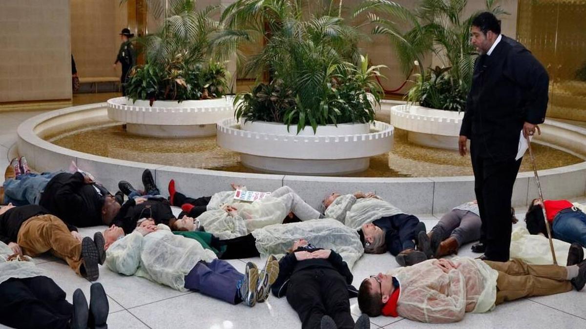 Rev. William Barber, standing, prays over 13 protesters who participated in a die-in at the state capitol in 2015 to protest the state’s continued denial of Medicaid expansion. All but 14 states have expanded Medicaid. Supporters say that more than 500,000 uninsured North Carolinians would benefit if NC did. 