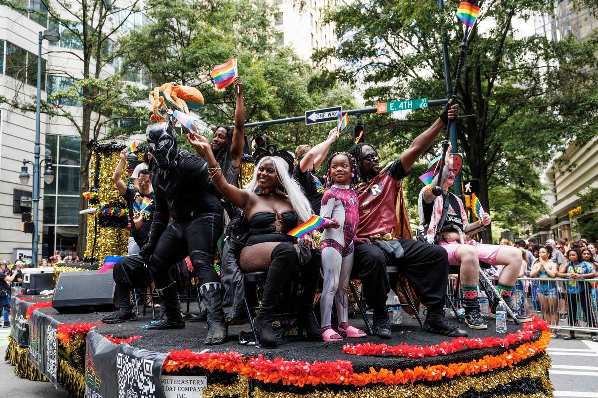 Members of the Charlotte Gaymers Network, dressed as superheros, wave rainbow flags and smile to the audience during the Charlotte Pride Festival & Parade on Sunday, Aug. 18, 2024