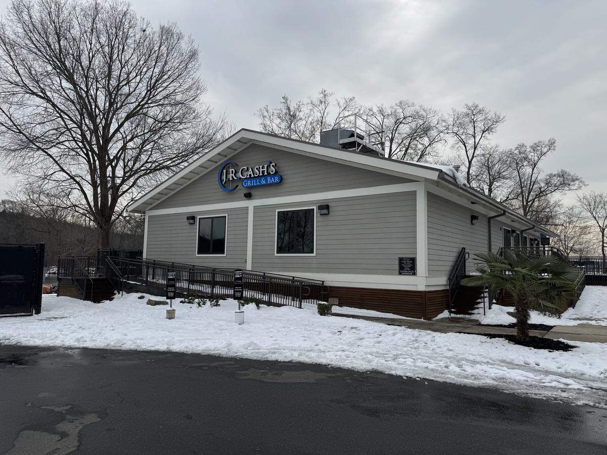 The exterior of J.R. Cash’s Grill & Bar, a gray siding building with a white roof, surrounded by a light layer of snow on the ground and a handicap-accessible ramp leading to the entrance.
