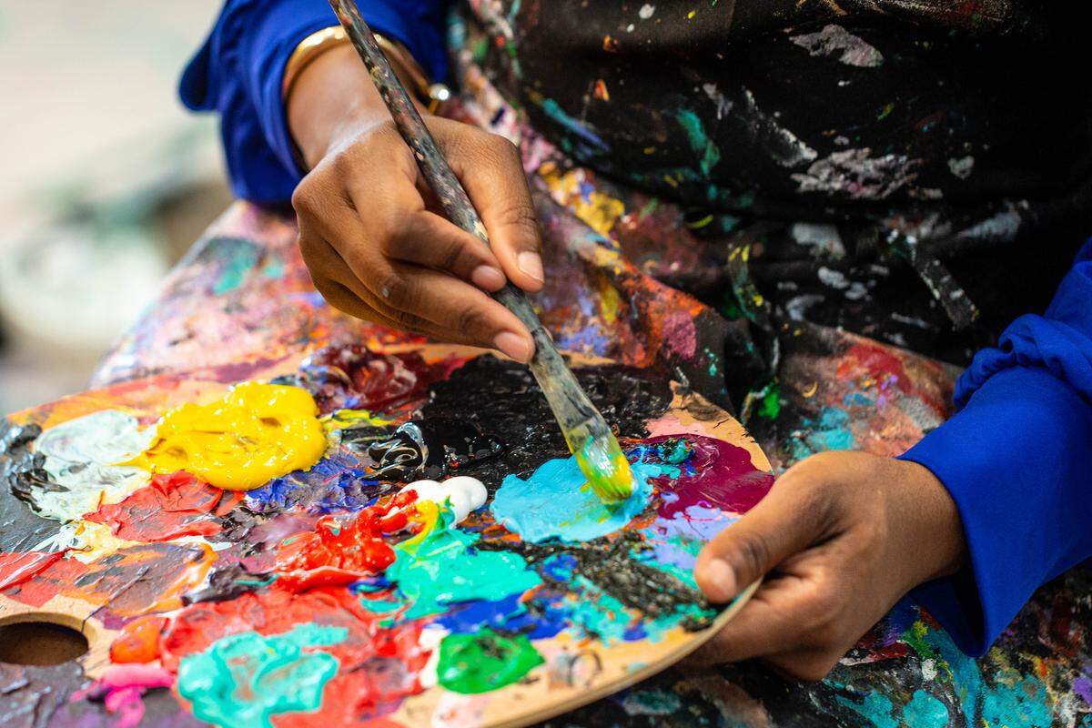 Charlotte artist Whitney Austin adds color to her brush as she works on one of her paintings. “I’m passionate about black beauty, culture, our history,” she says. “I want a little girl who likes to draw to see a picture on the wall that looks like her.”