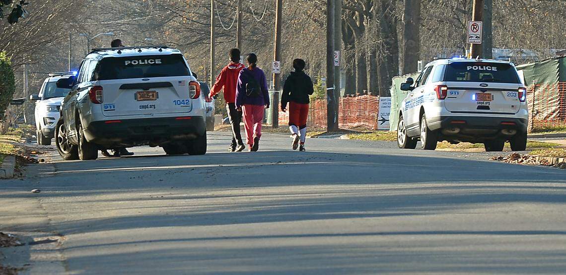 People walk past Charlotte-Mecklenburg police vehicles along Senior Drive outside West Charlotte High School on Monday, December 13, 2021. Officers remained at the school during student dismissal after a report of a gunshot on campus.