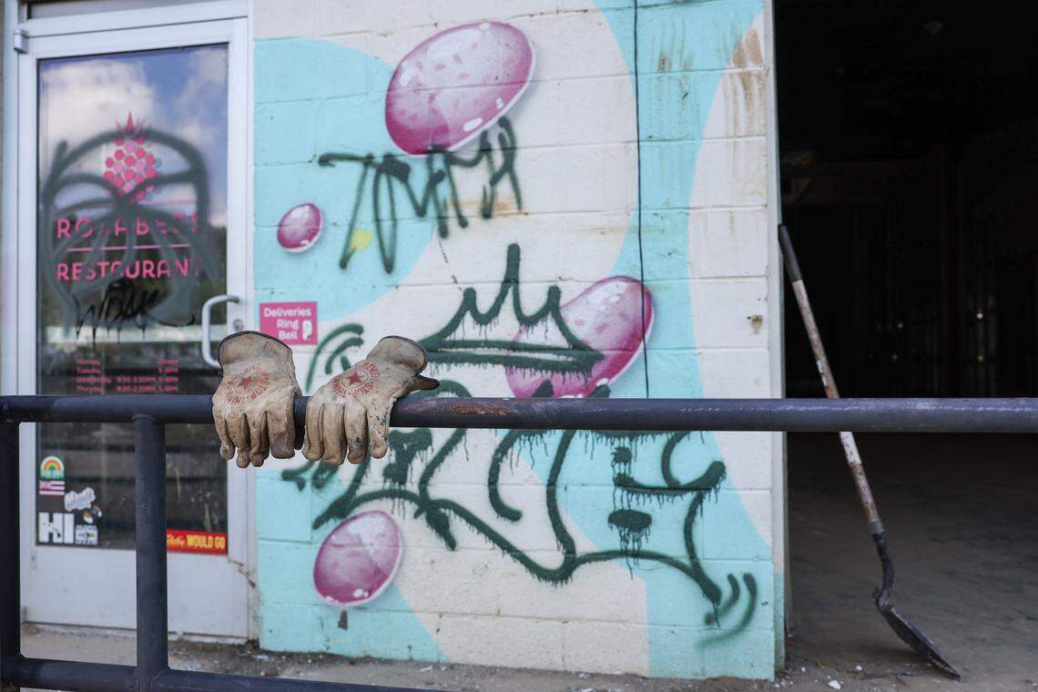 A worker’s gloves sit molded to the railing in front of Rosabees Restaurant in the River Arts District of Asheville, NC. The restaurant reamins closed, as do all other businesses in its vicinity, after historic flooding last year during Helene.